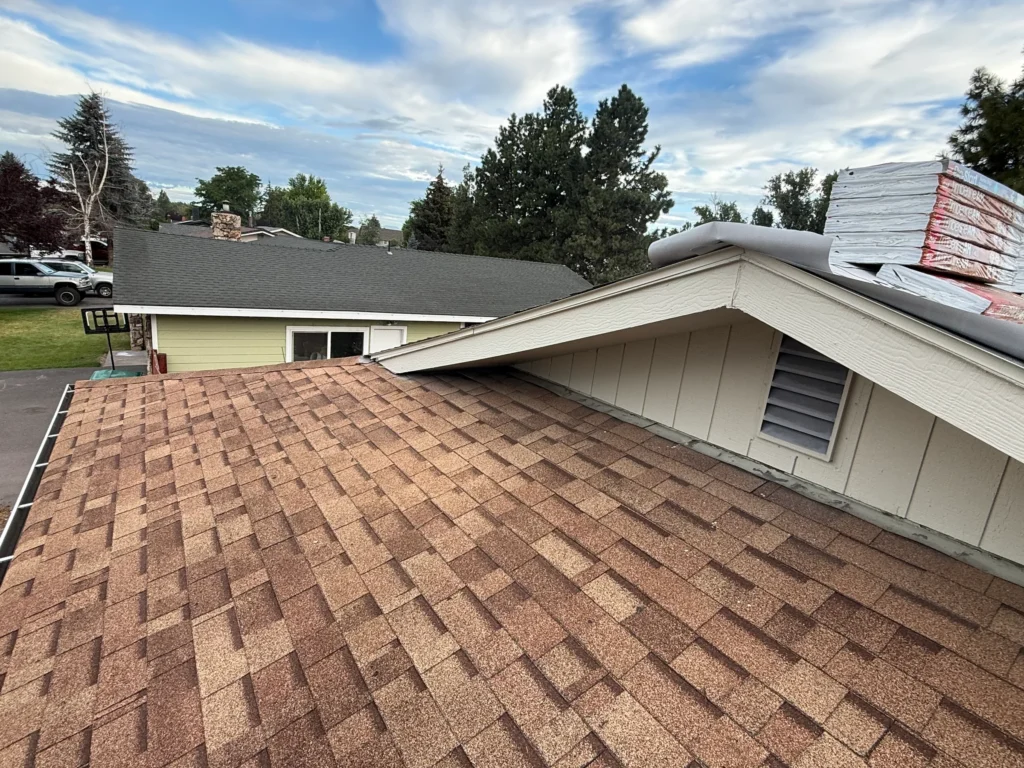 Roofing project with brown shingles and materials staged above a dormer