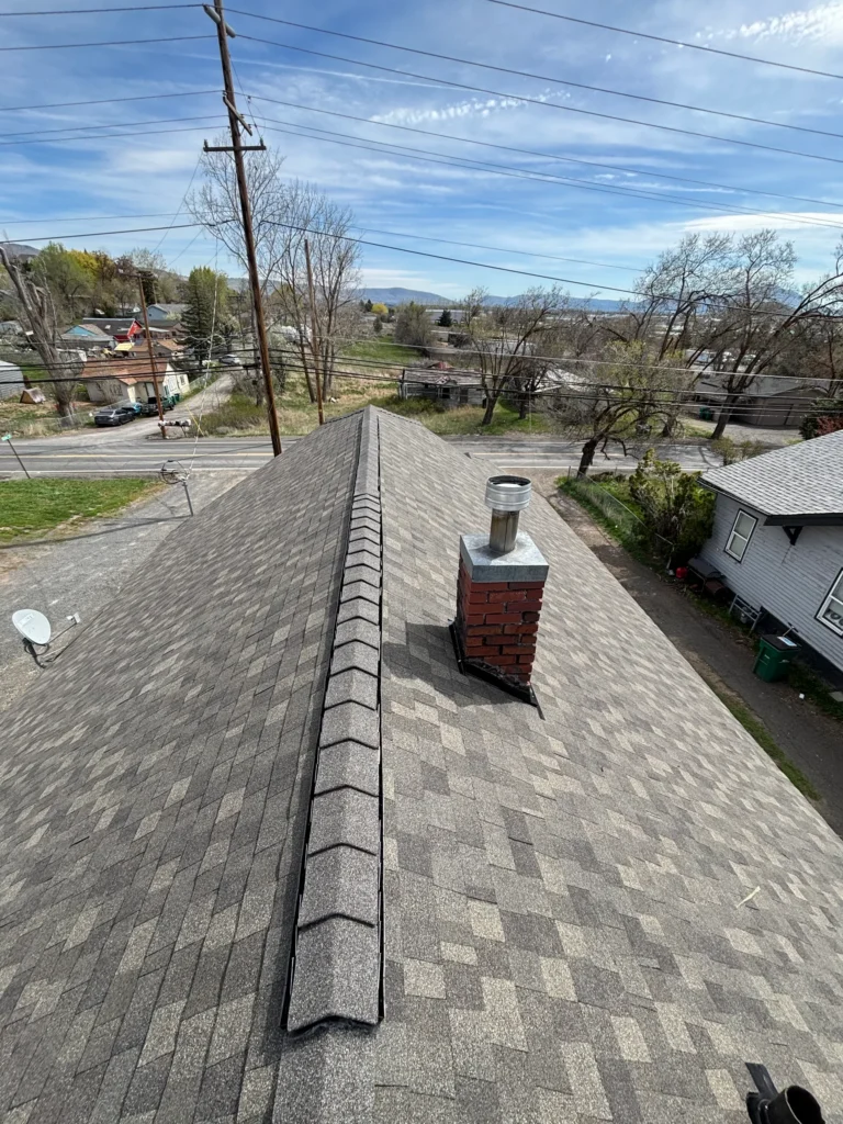 Finished shingle roof showing a ridge and flashing around a roof junction.