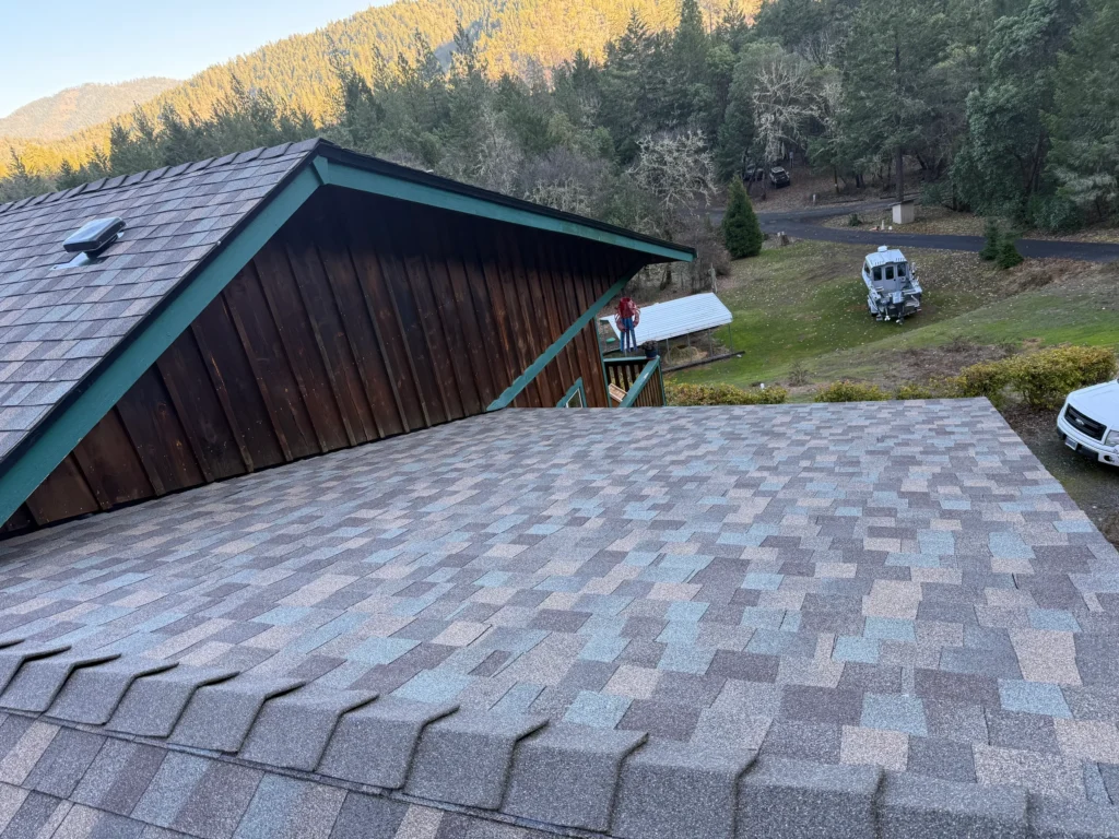 Shingle roof on a wood-sided home beneath a forested hillside