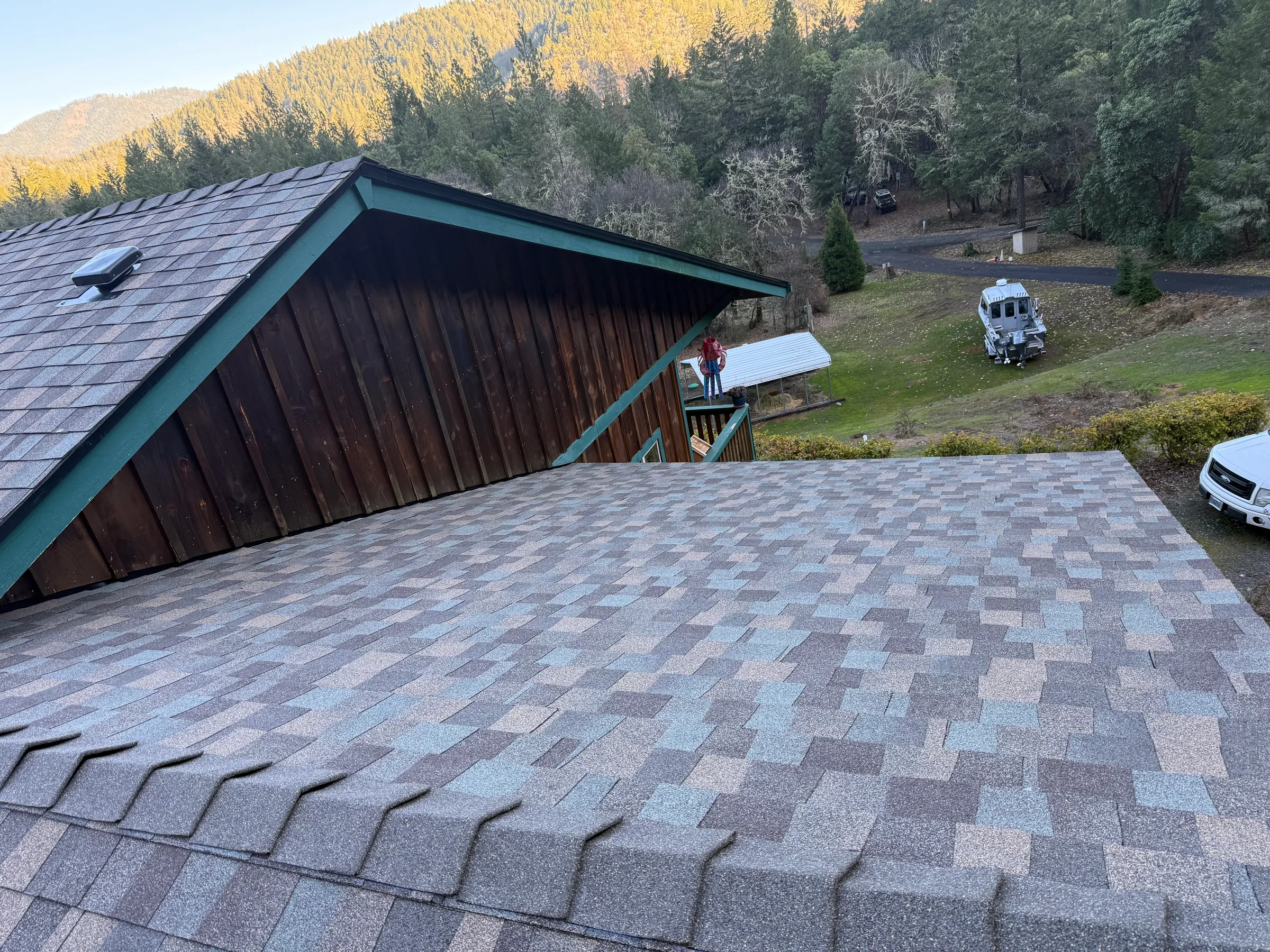 Shingle roof on a wood-sided home beneath a forested hillside
